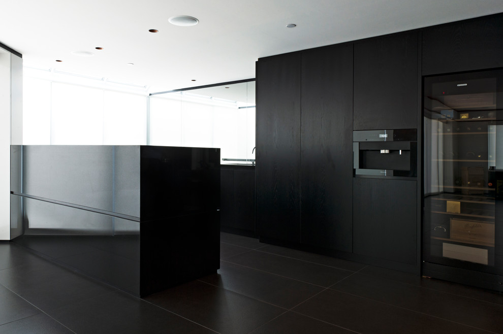 Foto på ett stort funkis linjärt kök och matrum, med en enkel diskho, släta luckor, svarta skåp, granitbänkskiva, spegel som stänkskydd, svarta vitvaror, klinkergolv i keramik, en köksö och svart golv