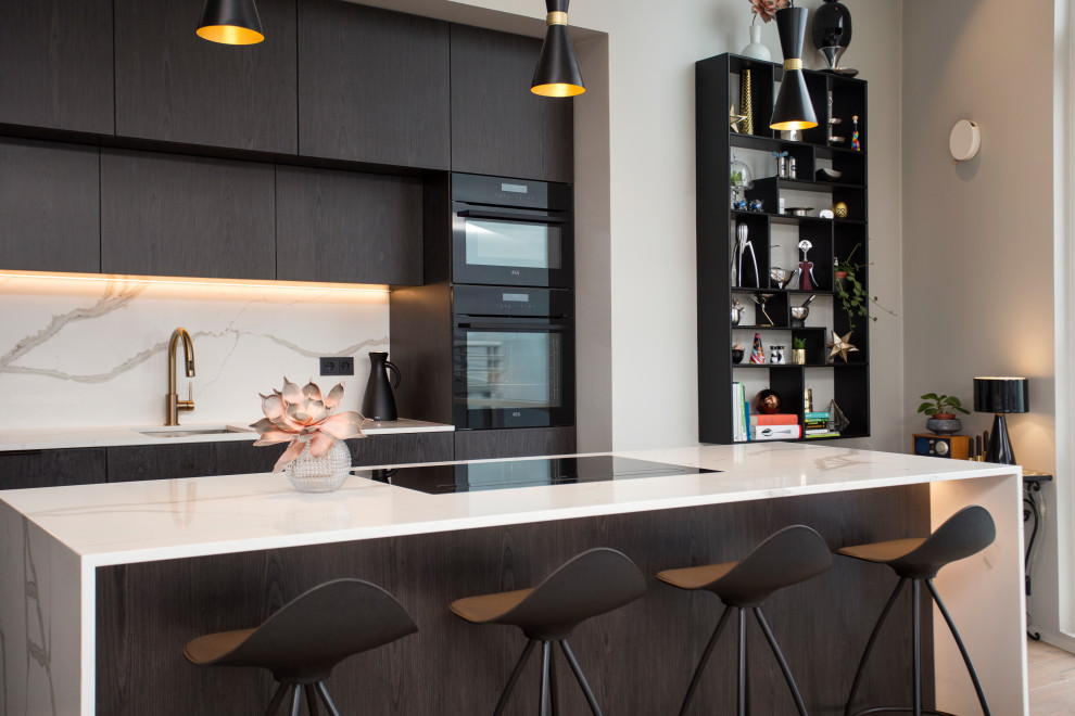 Cette image montre une petite cuisine américaine linéaire minimaliste avec un évier posé, un placard à porte plane, des portes de placard noires, plan de travail en marbre, une crédence grise, un électroménager noir, un sol en bois brun, îlot, un sol marron et un plan de travail blanc.