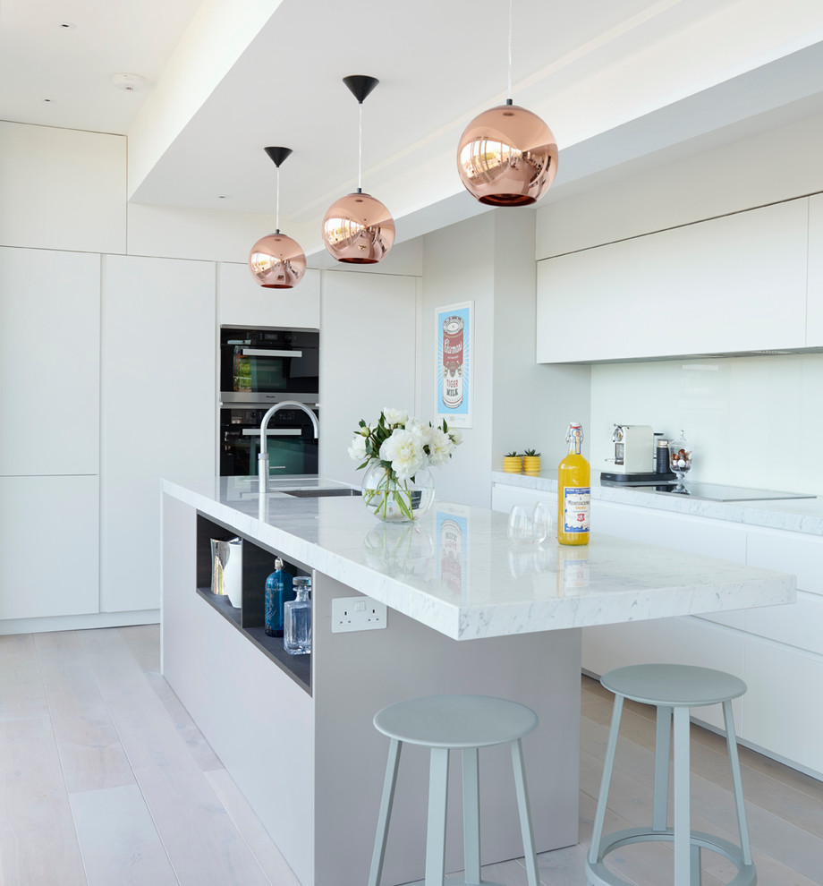 Moderne Küche mit Unterbauwaschbecken, flächenbündigen Schrankfronten, weißen Schränken, Küchenrückwand in Weiß, Glasrückwand und Kücheninsel in London
