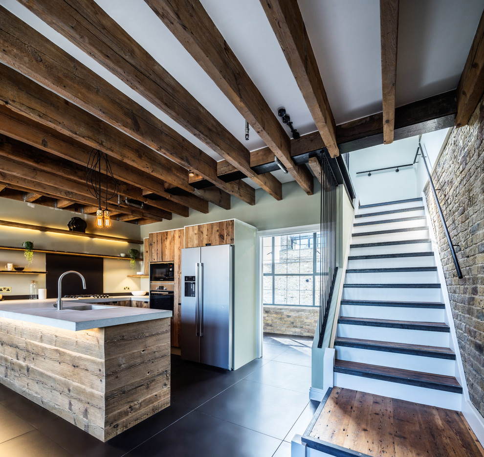 ロンドンにある高級な中くらいなラスティックスタイルのおしゃれなキッチン (フラットパネル扉のキャビネット、中間色木目調キャビネット、コンクリートカウンター、グレーのキッチンパネル、シルバーの調理設備、黒い床) の写真