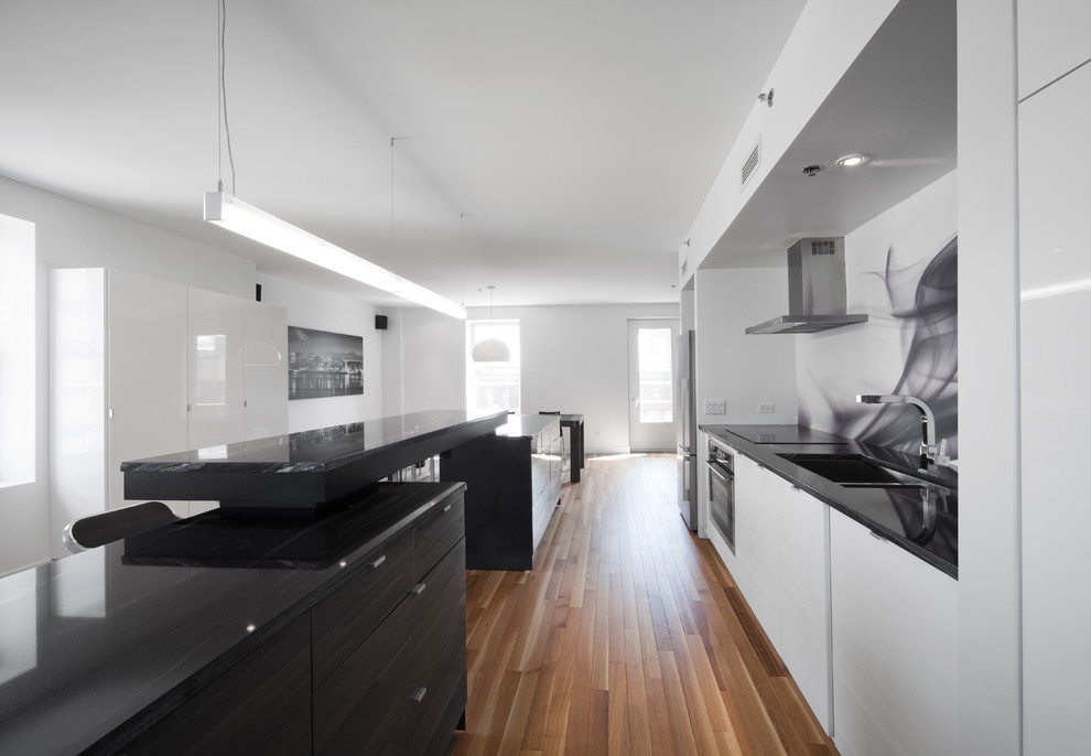 Пример оригинального дизайна: прямая кухня-гостиная в современном стиле с плоскими фасадами, черным фартуком, техникой из нержавеющей стали, фартуком из стекла и черно-белыми фасадами