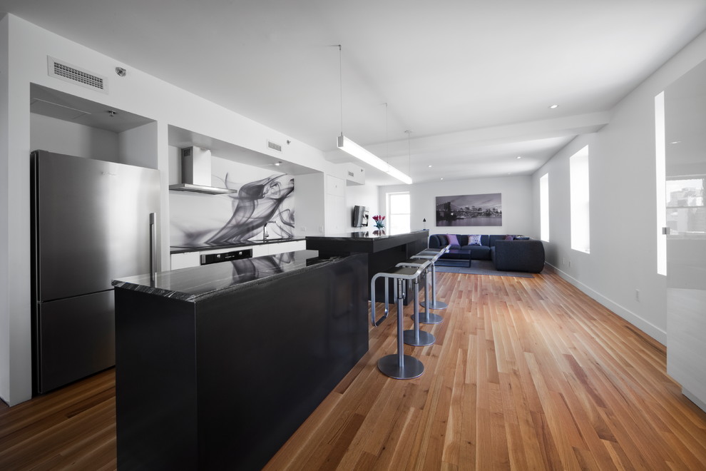 Contemporary single-wall open plan kitchen in Montreal with black splashback, stainless steel appliances, flat-panel cabinets and glass sheet splashback.