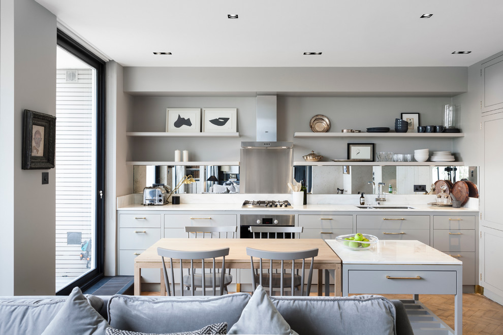 Bild på ett funkis linjärt kök med öppen planlösning, med en dubbel diskho, släta luckor, grå skåp, stänkskydd med metallisk yta, spegel som stänkskydd, rostfria vitvaror, mellanmörkt trägolv och en köksö