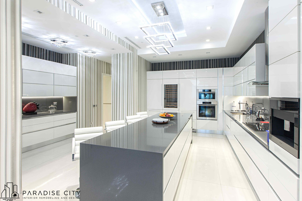 This is an example of a large contemporary u-shaped enclosed kitchen in Miami with a submerged sink, flat-panel cabinets, white cabinets, composite countertops, grey splashback, stone slab splashback, stainless steel appliances, porcelain flooring and an island.