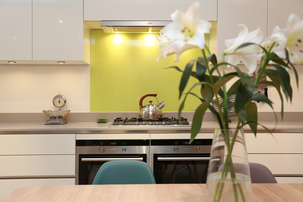 ロンドンにある広いコンテンポラリースタイルのおしゃれなLDK (ドロップインシンク、フラットパネル扉のキャビネット、白いキャビネット、クオーツストーンカウンター、黄色いキッチンパネル、ガラス板のキッチンパネル、パネルと同色の調理設備、アイランドなし、ベージュの床) の写真