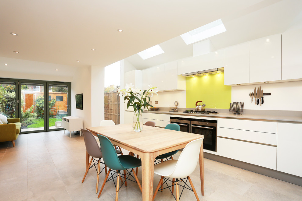 Example of a large trendy single-wall beige floor eat-in kitchen design in London with yellow backsplash, white cabinets, quartz countertops, glass sheet backsplash, stainless steel appliances and no island