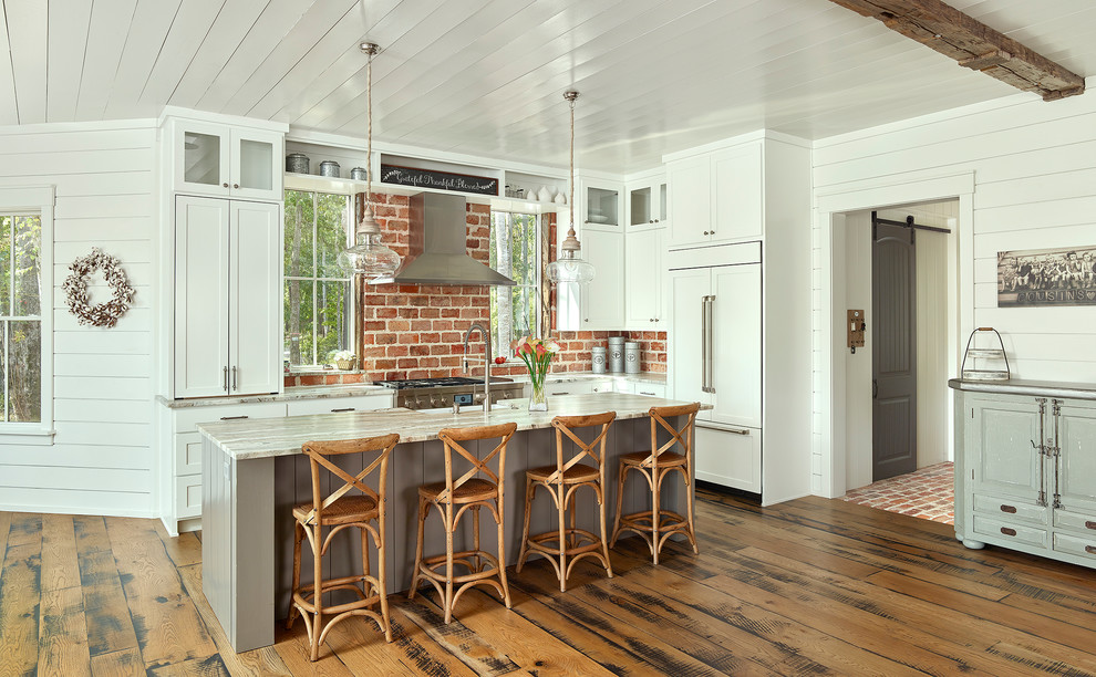 Foto på ett mellanstort lantligt l-kök, med en undermonterad diskho, luckor med infälld panel, vita skåp, bänkskiva i kvartsit, rött stänkskydd, stänkskydd i tegel, rostfria vitvaror, ljust trägolv, en köksö och brunt golv
