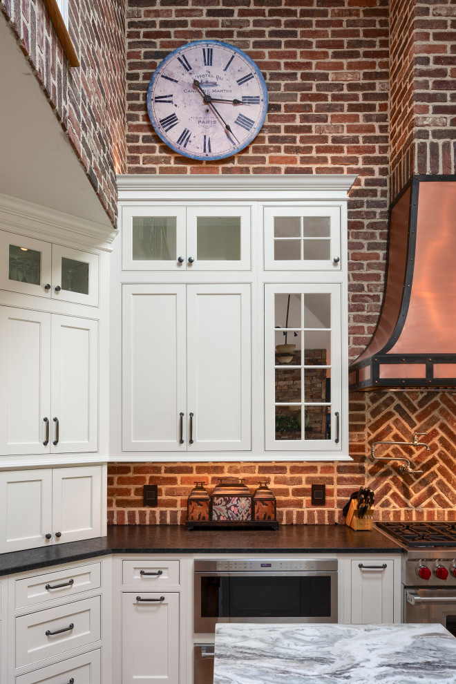 Eat-in kitchen - large rustic u-shaped light wood floor and brown floor eat-in kitchen idea in Other with white cabinets, brick backsplash, stainless steel appliances, an island, a farmhouse sink, recessed-panel cabinets, soapstone countertops, red backsplash and black countertops