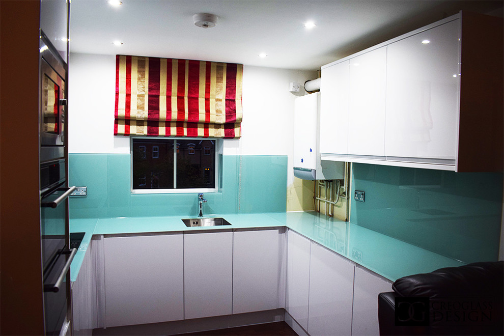 Große Moderne Wohnküche ohne Insel mit weißen Schränken, Küchenrückwand in Grün, Glasrückwand und grüner Arbeitsplatte in Hertfordshire