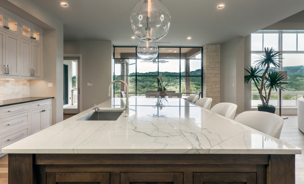 Design ideas for a classic kitchen in Austin with a submerged sink, recessed-panel cabinets, grey cabinets, quartz worktops, white splashback, stone tiled splashback, stainless steel appliances and light hardwood flooring.