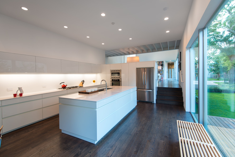 Moderne Küche in L-Form mit weißen Schränken, Quarzwerkstein-Arbeitsplatte, Küchenrückwand in Weiß, Kücheninsel, flächenbündigen Schrankfronten, Küchengeräten aus Edelstahl und dunklem Holzboden in Houston