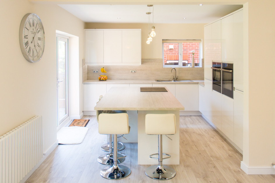 Immagine di un cucina con isola centrale minimalista di medie dimensioni con lavello da incasso, ante beige, top in laminato, paraspruzzi beige, elettrodomestici neri, pavimento in compensato, pavimento beige e top beige