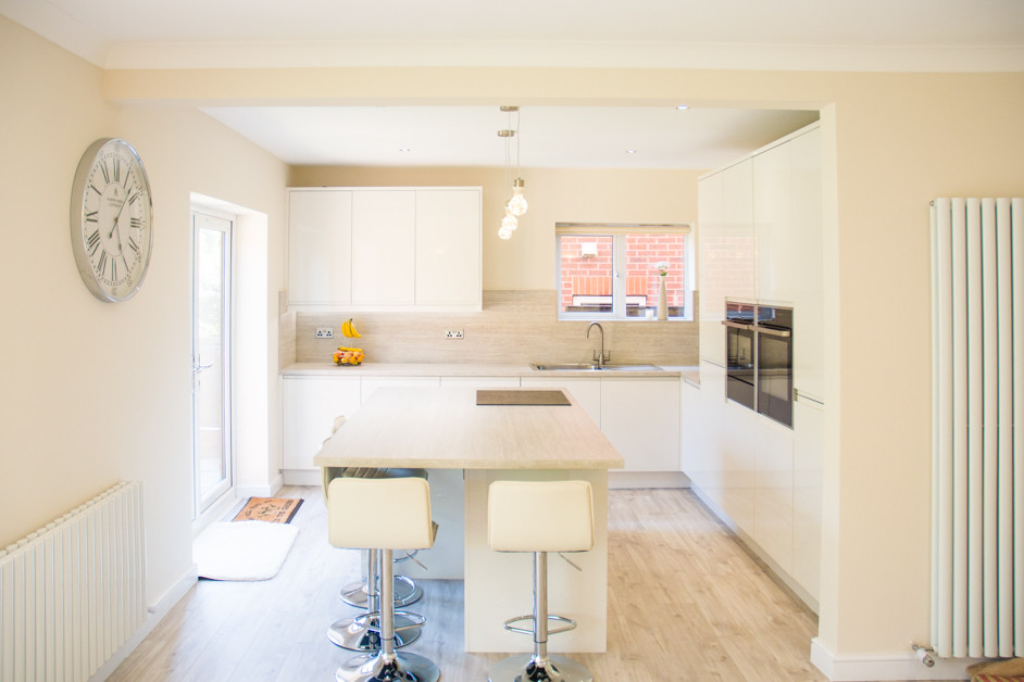Immagine di un cucina con isola centrale moderno di medie dimensioni con lavello da incasso, ante beige, top in laminato, paraspruzzi beige, elettrodomestici neri, pavimento in compensato, pavimento beige e top beige