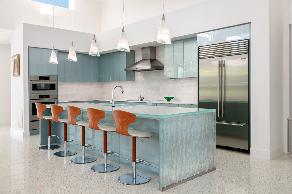Foto på ett stort funkis blå l-kök, med en undermonterad diskho, släta luckor, blå skåp, bänkskiva i glas, vitt stänkskydd, stänkskydd i keramik, rostfria vitvaror, terrazzogolv, en köksö och flerfärgat golv