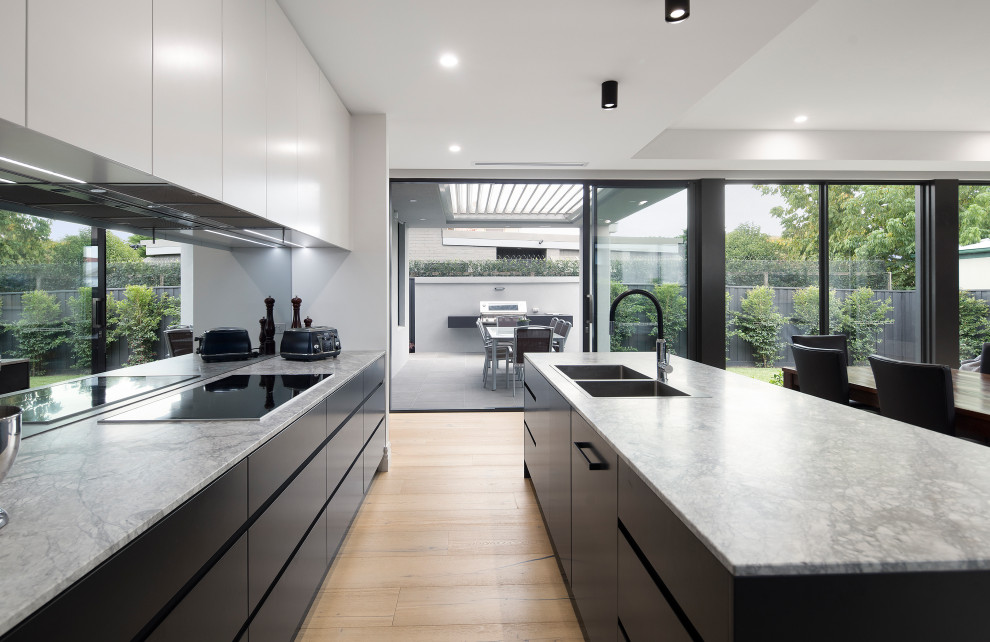 Réalisation d'une cuisine ouverte parallèle design de taille moyenne avec un placard à porte plane, des portes de placard noires, un plan de travail en quartz modifié, îlot et un plan de travail gris.