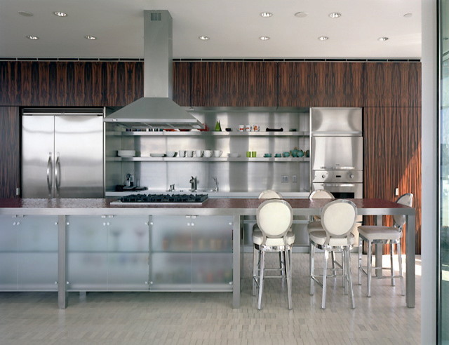 This is an example of a medium sized contemporary galley open plan kitchen in New York with a submerged sink, glass-front cabinets, dark wood cabinets, tile countertops, metallic splashback, stone slab splashback, stainless steel appliances, light hardwood flooring, an island and beige floors.