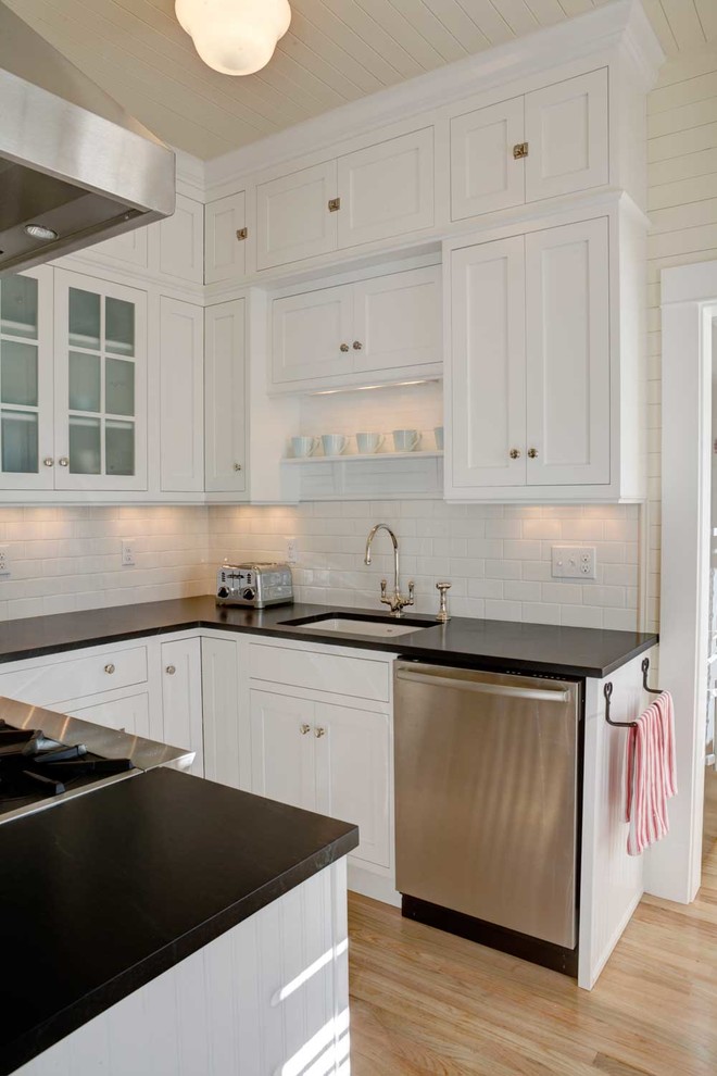 Modern inredning av ett litet kök, med rostfria vitvaror, en enkel diskho, luckor med infälld panel, vita skåp, bänkskiva i koppar, vitt stänkskydd, stänkskydd i keramik och ljust trägolv