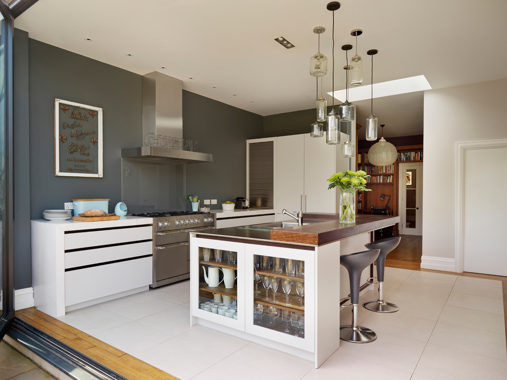 Cette photo montre une cuisine parallèle tendance avec un placard à porte plane, des portes de placard blanches, un électroménager en acier inoxydable et îlot.