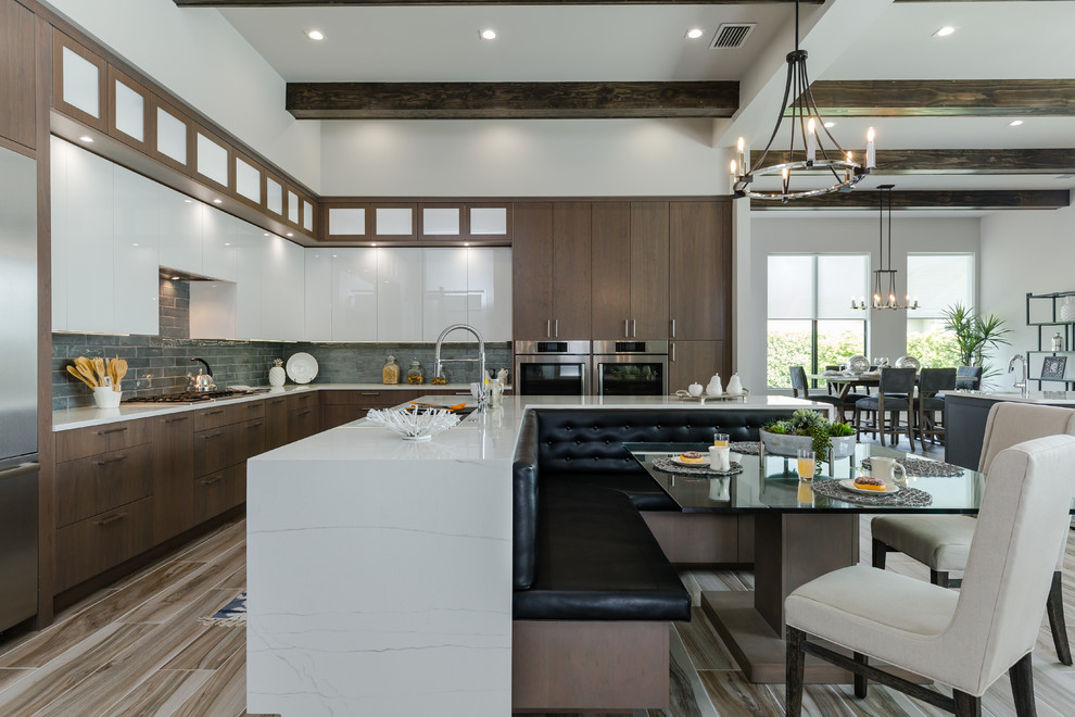 Modern inredning av ett vit vitt kök, med en undermonterad diskho, släta luckor, skåp i mellenmörkt trä, bänkskiva i kvarts, blått stänkskydd, stänkskydd i glaskakel, rostfria vitvaror, en köksö och flerfärgat golv