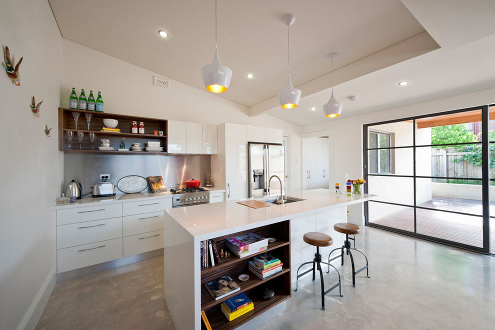 Photo of a contemporary galley kitchen in Perth with a submerged sink, flat-panel cabinets, white cabinets, metallic splashback, stainless steel appliances, concrete flooring and an island.