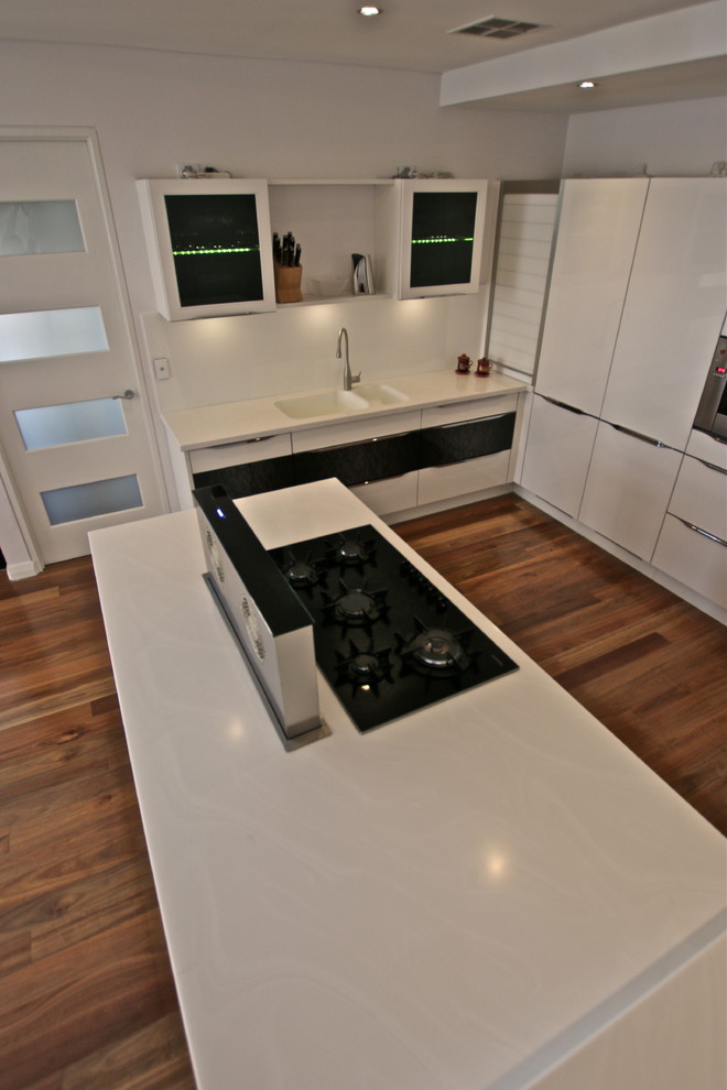 Foto di una grande cucina moderna con lavello integrato, ante lisce, ante bianche, top in superficie solida, paraspruzzi bianco, paraspruzzi con lastra di vetro, elettrodomestici neri e pavimento in legno massello medio
