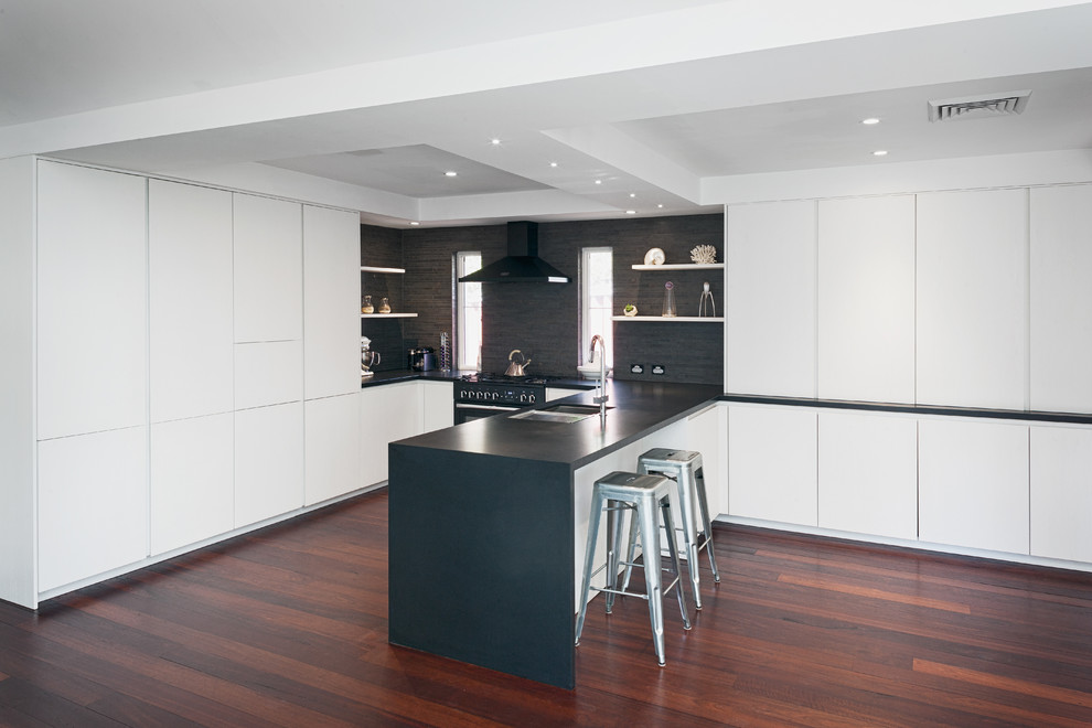 Esempio di una grande cucina minimalista con ante bianche, top in granito, paraspruzzi nero, paraspruzzi con piastrelle in ceramica, elettrodomestici neri e pavimento in legno massello medio