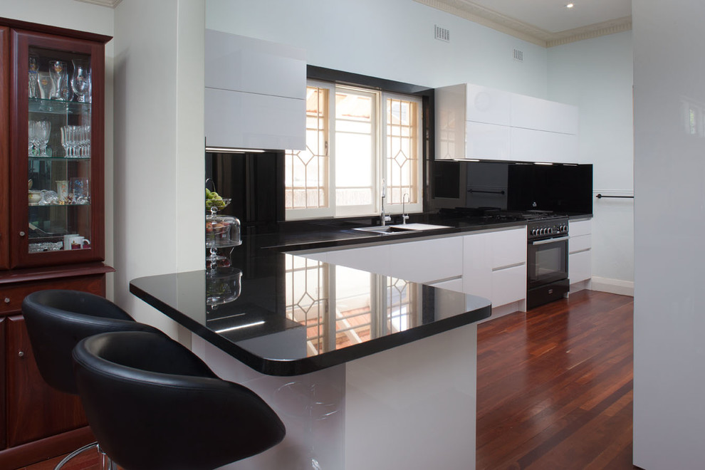 Exempel på ett mellanstort modernt kök, med en dubbel diskho, vita skåp, granitbänkskiva, svart stänkskydd, stänkskydd i glaskakel, svarta vitvaror, mellanmörkt trägolv och en köksö