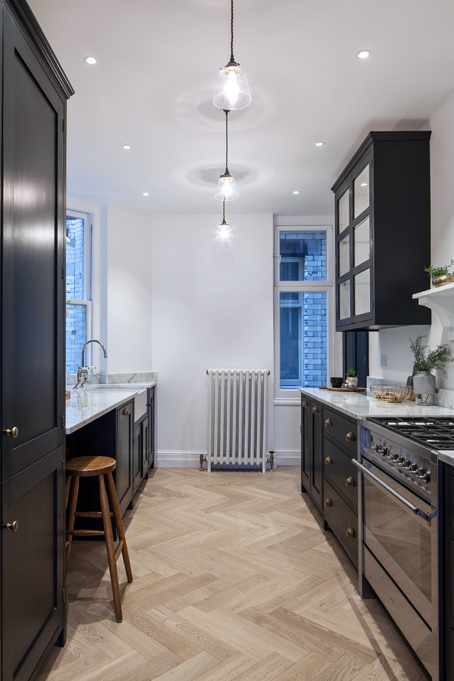 Inspiration for a medium sized rural galley kitchen in London with shaker cabinets, marble worktops, stainless steel appliances, a belfast sink, black cabinets, light hardwood flooring, no island, beige floors and white worktops.