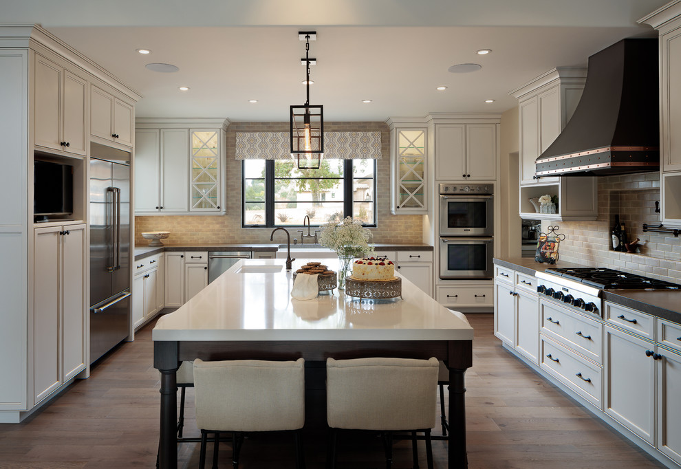 Photo of a large classic u-shaped kitchen/diner in San Francisco with a belfast sink, beaded cabinets, white cabinets, soapstone worktops, grey splashback, stainless steel appliances, light hardwood flooring, an island and brown floors.