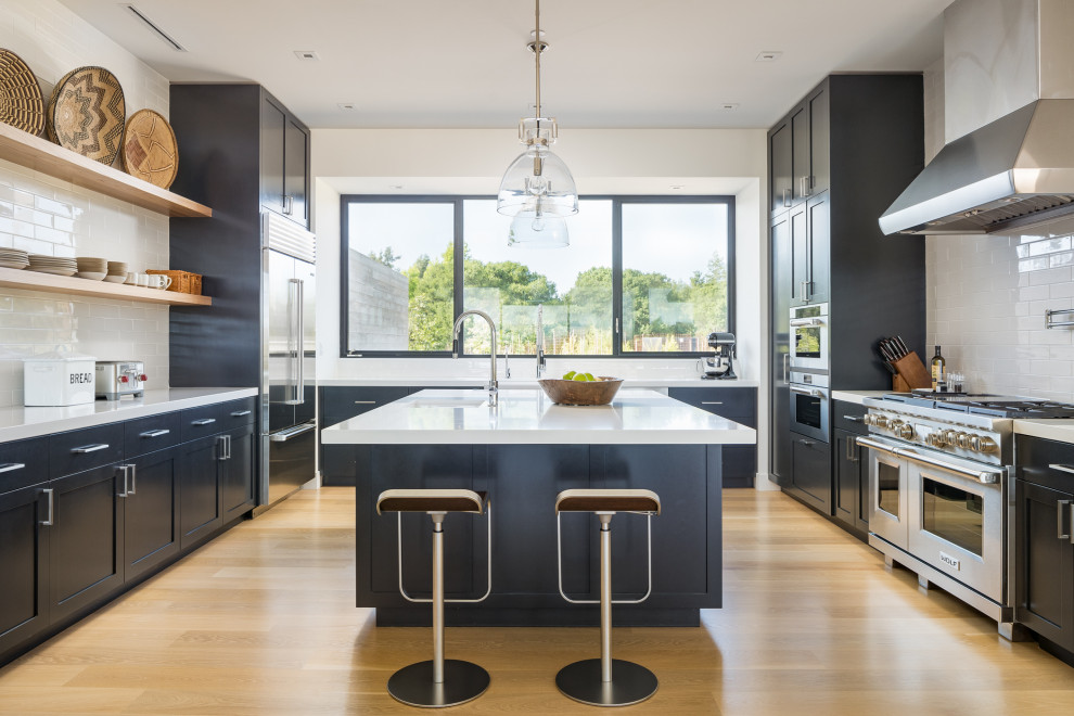 Immagine di una cucina classica con lavello sottopiano, ante in stile shaker, ante nere, elettrodomestici in acciaio inossidabile, pavimento in legno massello medio, pavimento marrone e top bianco