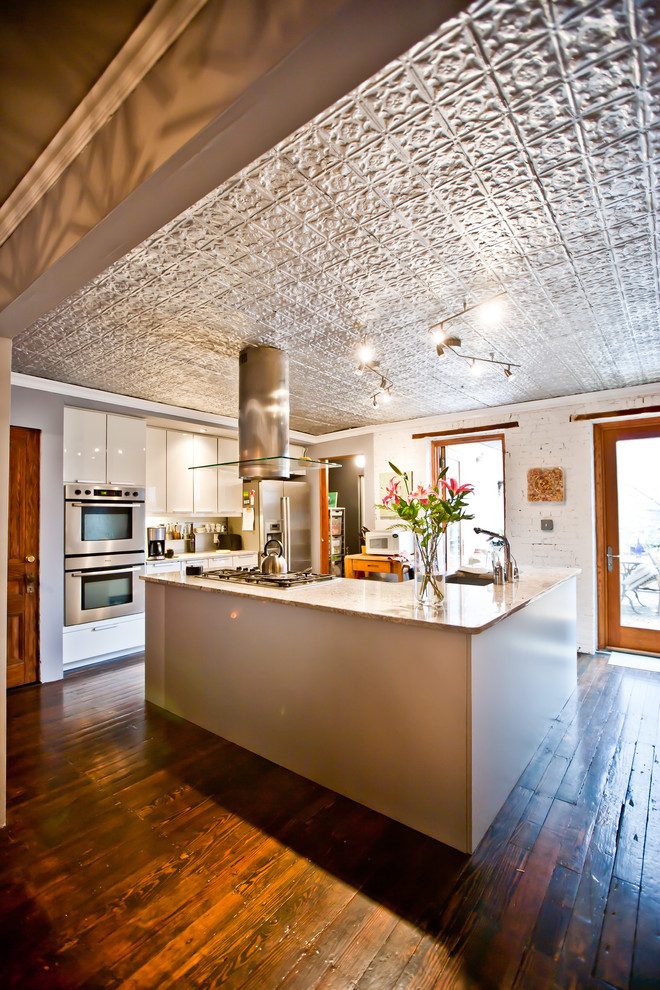Urige Küche mit Marmor-Arbeitsplatte, Küchengeräten aus Edelstahl, flächenbündigen Schrankfronten, weißen Schränken und Mauersteinen in New York