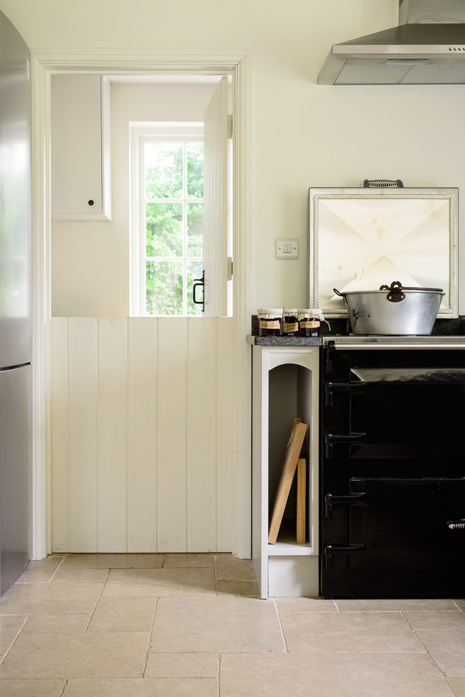Foto på ett mellanstort lantligt kök och matrum, med en rustik diskho, skåp i shakerstil, grå skåp, granitbänkskiva, svarta vitvaror, kalkstensgolv och en halv köksö