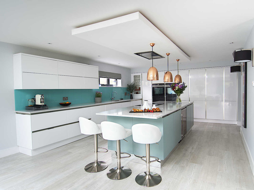 Design ideas for a large contemporary galley open plan kitchen in Hampshire with an integrated sink, flat-panel cabinets, white cabinets, composite countertops, blue splashback, glass sheet splashback, stainless steel appliances, porcelain flooring, an island and grey floors.