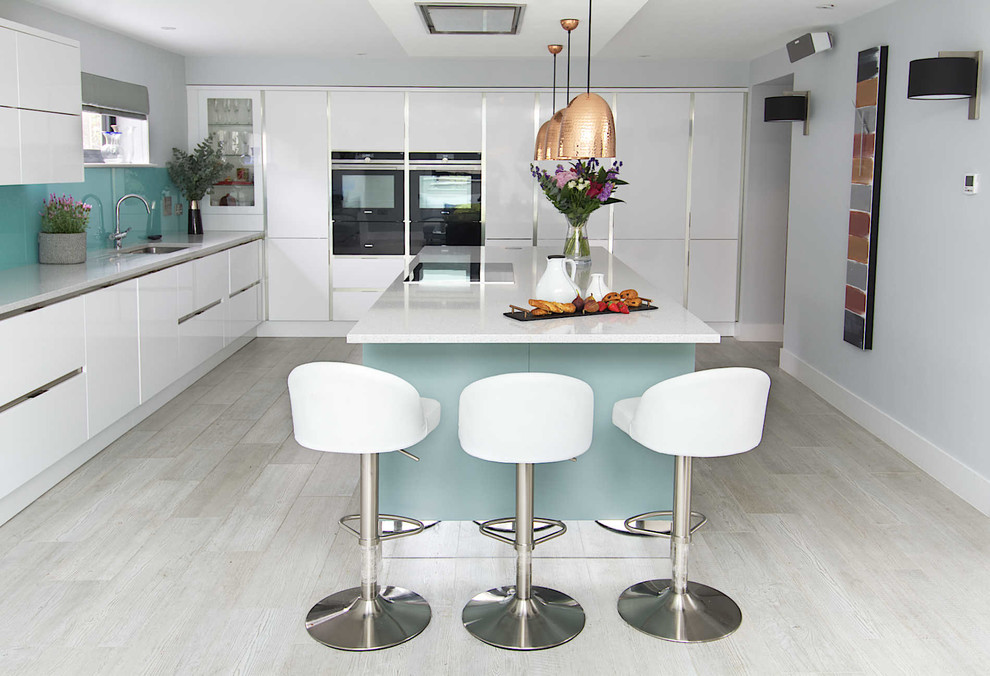 Photo of a large contemporary galley open plan kitchen in Hampshire with an integrated sink, flat-panel cabinets, white cabinets, composite countertops, blue splashback, glass sheet splashback, stainless steel appliances, porcelain flooring, an island and grey floors.
