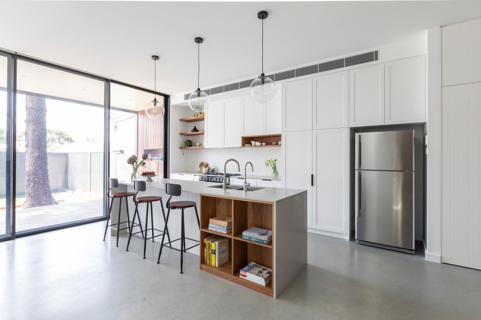Medium sized classic single-wall open plan kitchen in Sydney with a submerged sink, shaker cabinets, white cabinets, engineered stone countertops, white splashback, ceramic splashback, black appliances, concrete flooring, an island, grey floors and grey worktops.