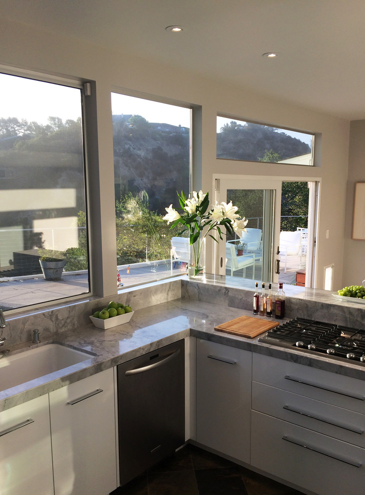 Bild på ett stort funkis kök, med en undermonterad diskho, släta luckor, vita skåp, marmorbänkskiva, fönster som stänkskydd, rostfria vitvaror, skiffergolv och en halv köksö