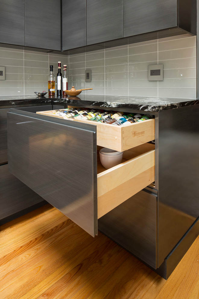 Contemporary kitchen in Minneapolis with a submerged sink, flat-panel cabinets, grey cabinets, granite worktops, grey splashback, glass tiled splashback, stainless steel appliances, light hardwood flooring and a breakfast bar.