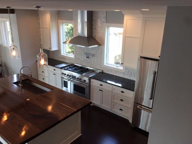 Klassisk inredning av ett mellanstort svart svart kök, med en undermonterad diskho, luckor med infälld panel, vita skåp, granitbänkskiva, vitt stänkskydd, stänkskydd i stenkakel, rostfria vitvaror, mörkt trägolv, en köksö och brunt golv