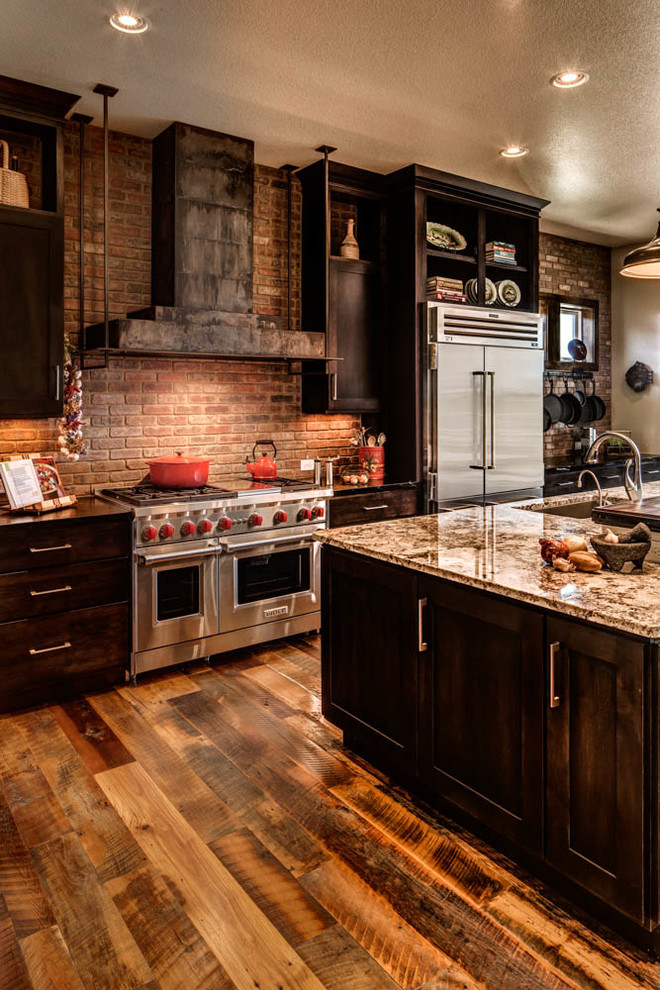 Foto på ett stort rustikt svart l-kök, med en undermonterad diskho, skåp i shakerstil, skåp i mörkt trä, rött stänkskydd, stänkskydd i tegel, rostfria vitvaror, mellanmörkt trägolv, en köksö och brunt golv