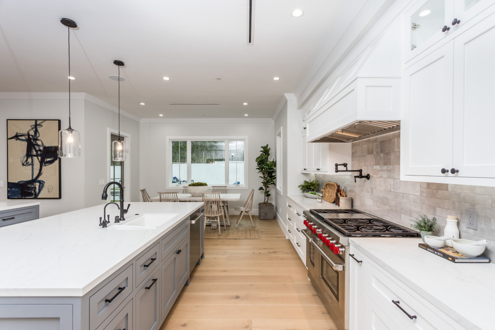 Expansive classic galley open plan kitchen in Los Angeles with a submerged sink, shaker cabinets, white cabinets, grey splashback, stone tiled splashback, stainless steel appliances, light hardwood flooring, multiple islands, beige floors, white worktops and a drop ceiling.