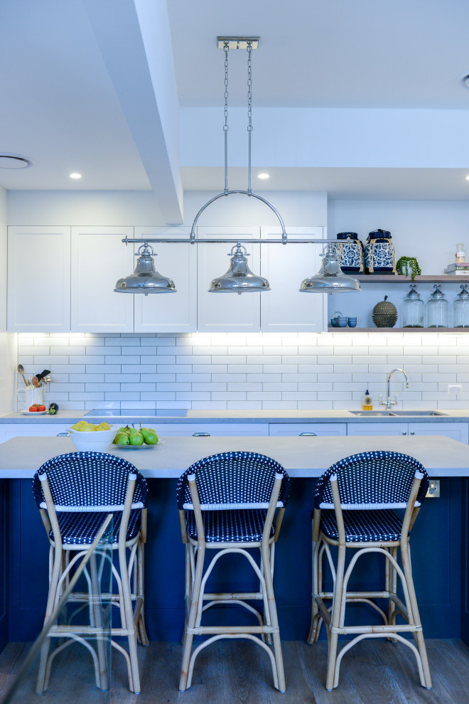 Foto på ett stort funkis grå kök, med en dubbel diskho, skåp i shakerstil, blå skåp, bänkskiva i kvarts, vitt stänkskydd, stänkskydd i tunnelbanekakel, rostfria vitvaror, mellanmörkt trägolv, en köksö och brunt golv
