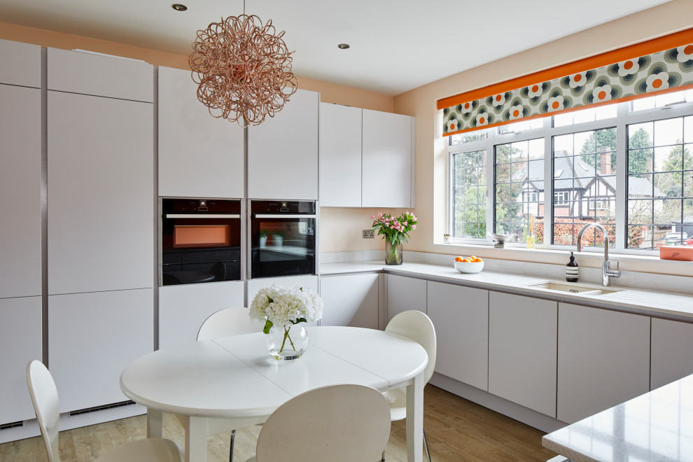 Photo of a medium sized contemporary u-shaped kitchen/diner in Kent with flat-panel cabinets, no island, white worktops, a submerged sink, white cabinets, white splashback, integrated appliances, medium hardwood flooring and beige floors.