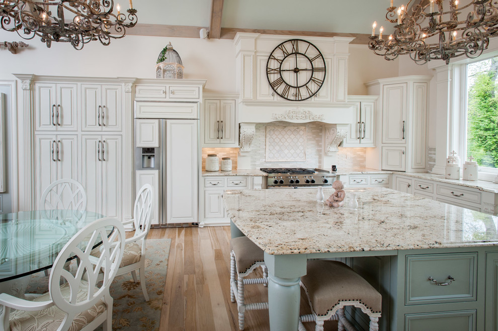 Bild på ett lantligt kök, med en nedsänkt diskho, luckor med upphöjd panel, vita skåp, granitbänkskiva, vitt stänkskydd, stänkskydd i keramik, rostfria vitvaror, ljust trägolv och en köksö