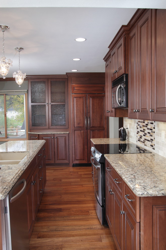 Eat-in kitchen - traditional galley eat-in kitchen idea in Milwaukee with an undermount sink, raised-panel cabinets, medium tone wood cabinets, quartz countertops, gray backsplash, stone tile backsplash and stainless steel appliances