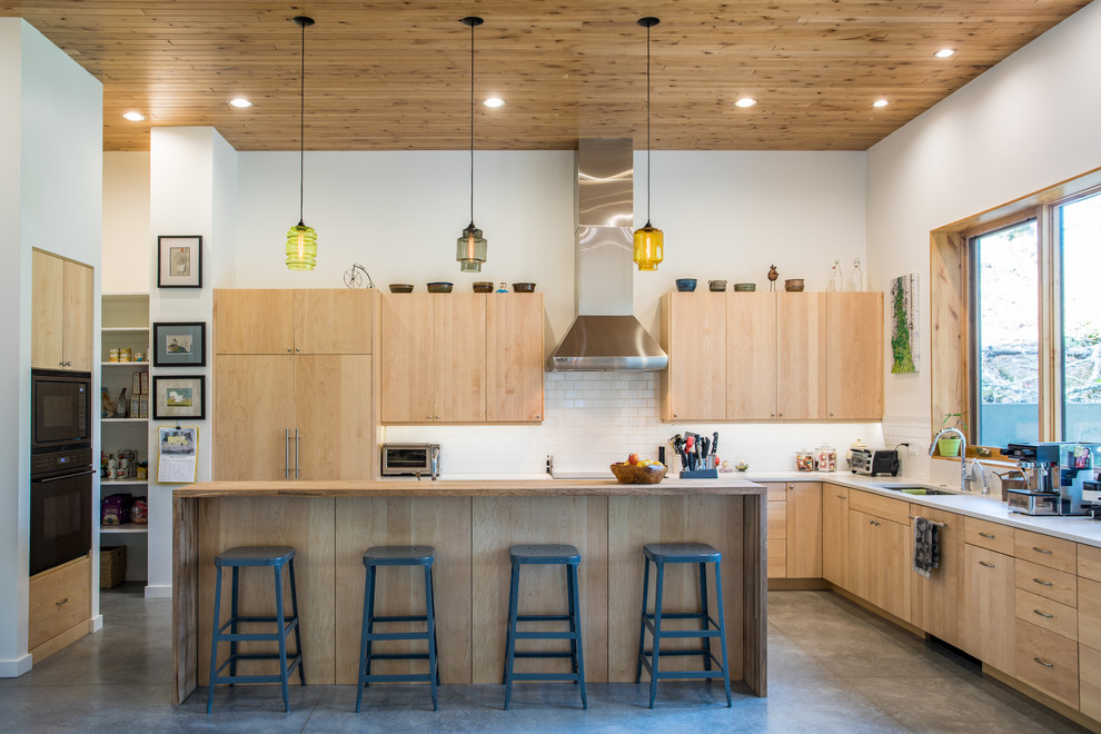 Example of a trendy u-shaped concrete floor and gray floor kitchen design in Portland with an undermount sink, flat-panel cabinets, light wood cabinets, white backsplash, subway tile backsplash, black appliances, an island and white countertops