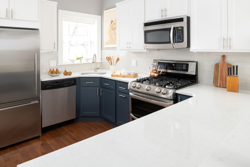 Bild på ett mellanstort funkis vit vitt kök, med en enkel diskho, släta luckor, blå skåp, bänkskiva i kvartsit, vitt stänkskydd, stänkskydd i keramik, rostfria vitvaror, mörkt trägolv och brunt golv