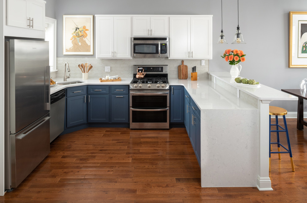 Inredning av ett modernt mellanstort vit vitt kök, med en enkel diskho, blå skåp, bänkskiva i kvartsit, vitt stänkskydd, stänkskydd i keramik, rostfria vitvaror, mörkt trägolv, brunt golv och skåp i shakerstil