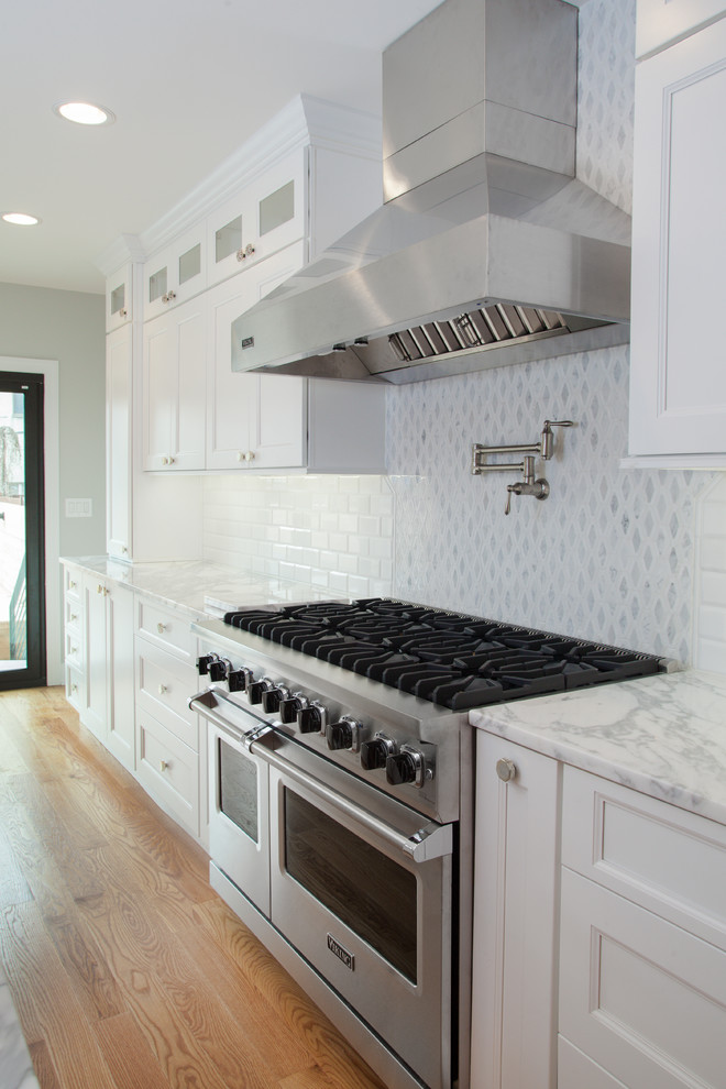 Example of a mid-sized transitional galley light wood floor and brown floor open concept kitchen design in Philadelphia with an undermount sink, recessed-panel cabinets, white cabinets, marble countertops, white backsplash, marble backsplash, stainless steel appliances, an island and white countertops