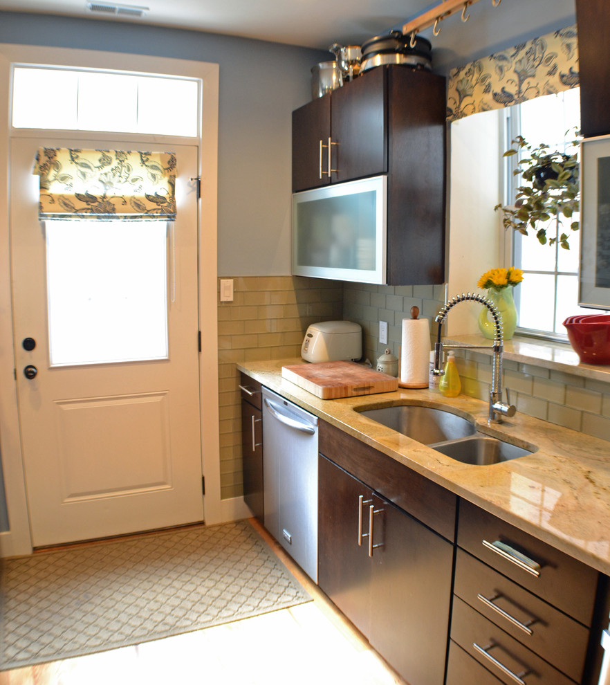 Bild på ett litet funkis kök, med en dubbel diskho, släta luckor, skåp i mörkt trä, granitbänkskiva, grönt stänkskydd, stänkskydd i tunnelbanekakel, rostfria vitvaror och ljust trägolv