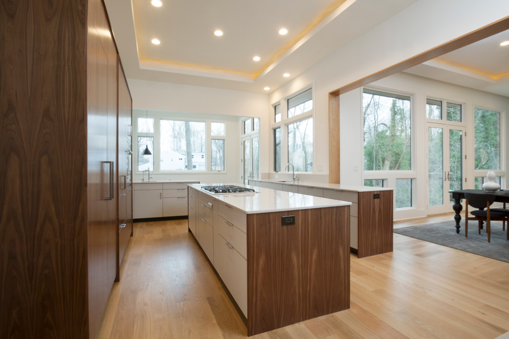 Large trendy u-shaped light wood floor and brown floor eat-in kitchen photo in New York with an undermount sink, flat-panel cabinets, solid surface countertops, white backsplash, stone slab backsplash, paneled appliances, an island and white cabinets